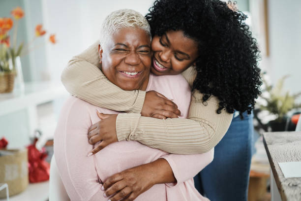 A grown woman hugging an older relative from behind, both women are smiling with joy.